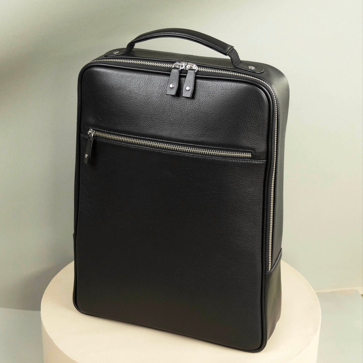 A black leather backpack with a top handle, zippered closure