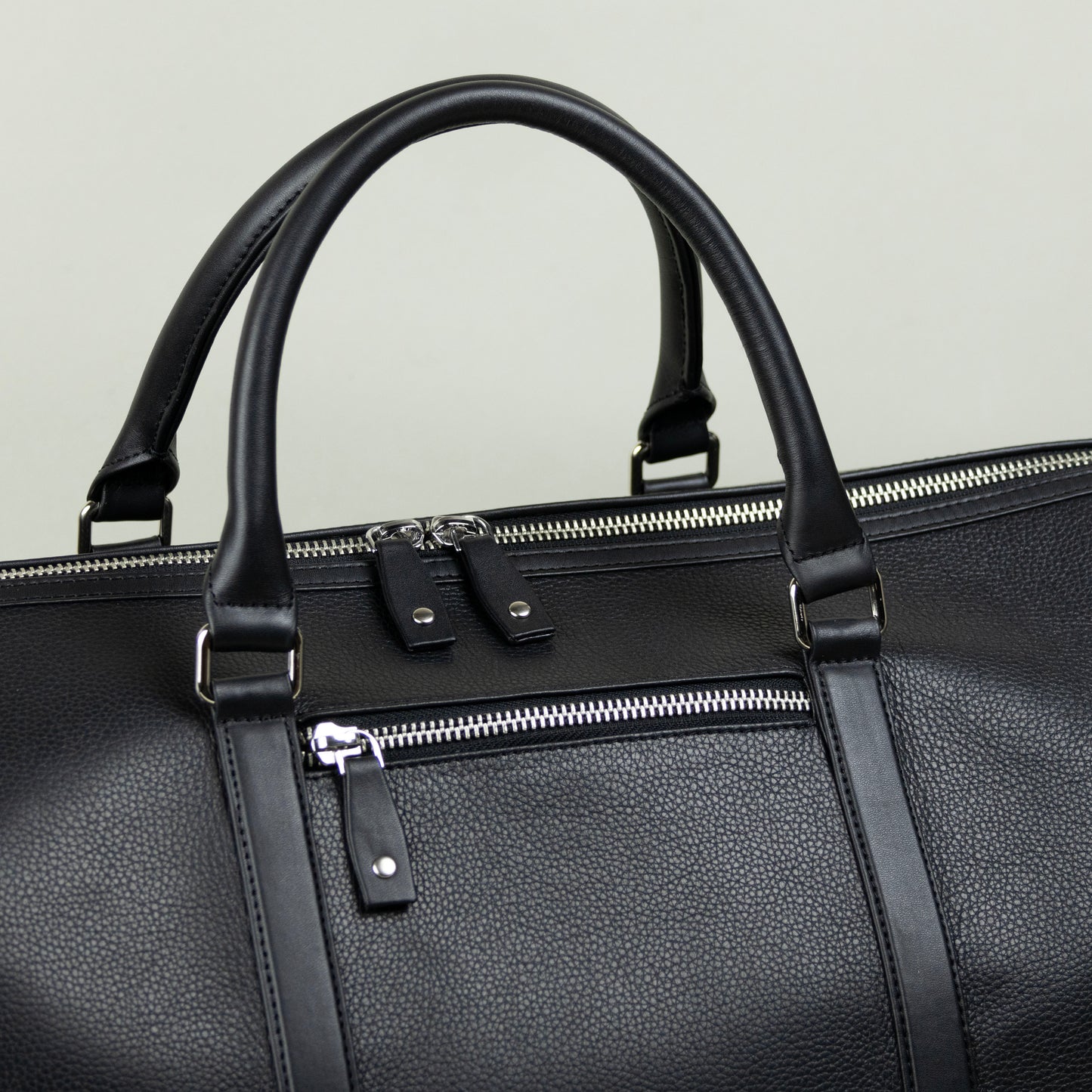 Black leather bag with handles and zippers on a light gray background