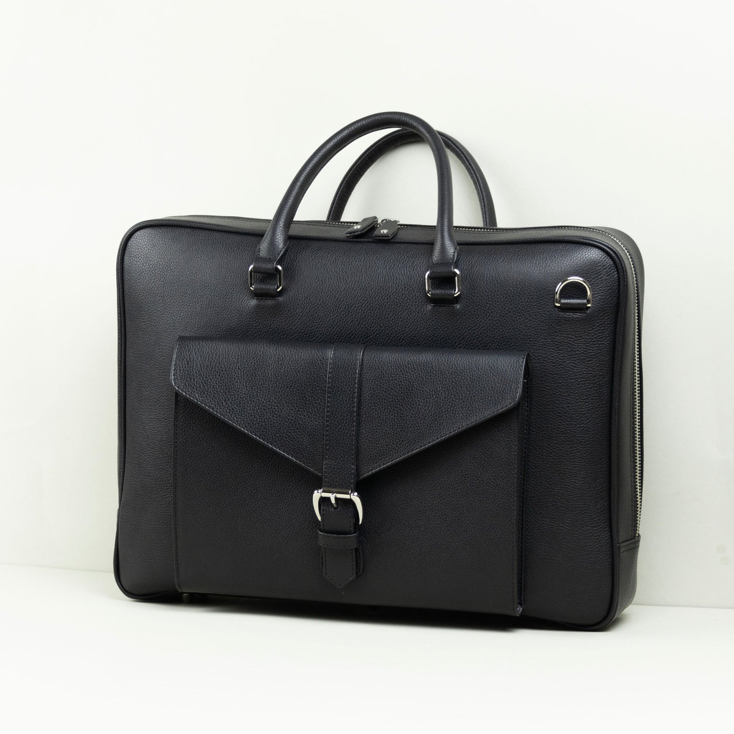 A black leather briefcase with dual top handles, a front flap pocket with a buckle closure, and silver-tone hardware, photographed on a white surface against a white wall.